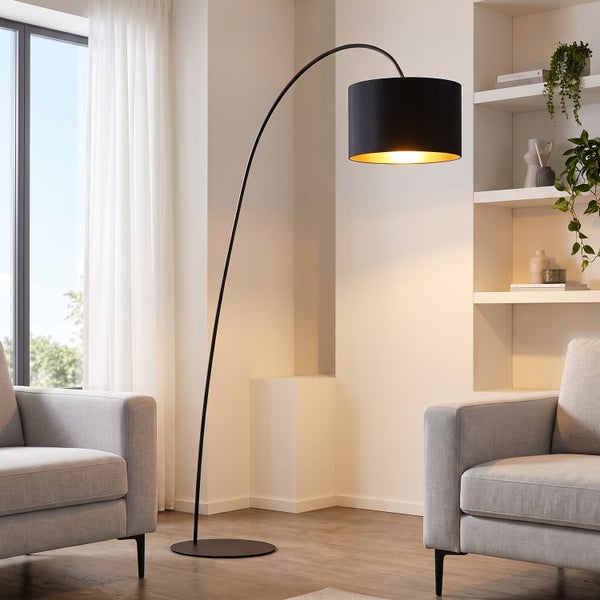 Moderne Bogenlampe mit geschwungenem Gestell und zylindrischem Lampenschirm in einem stilvollen Wohnzimmer mit Sesseln und Regalen.