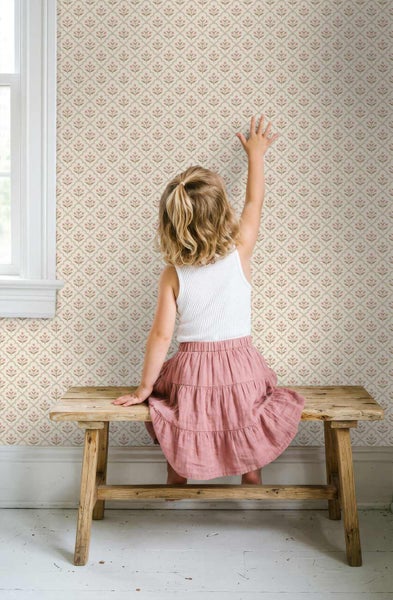 Kind auf Holzbank vor Wand mit romantischer Blumentapete mit kleinem Blütenmuster in hellem Kinderzimmer.