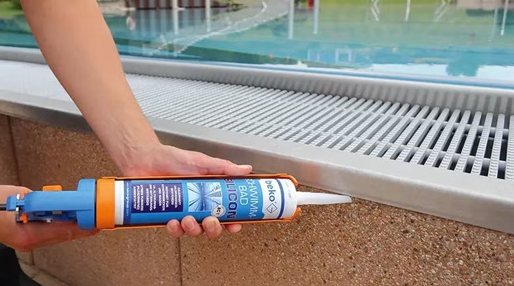 Eine Person verwendet eine Kartuschenpistole mit beko Schwimmbad Silikon zur Abdichtung an einem Schwimmbeckenrand.