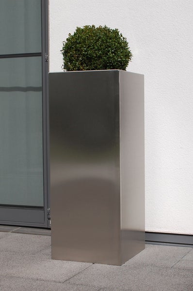 Hoher rechteckiger Pflanzkübel aus Edelstahl mit einem grünen Buchsbaum auf einer Terrasse vor einer Hauswand.