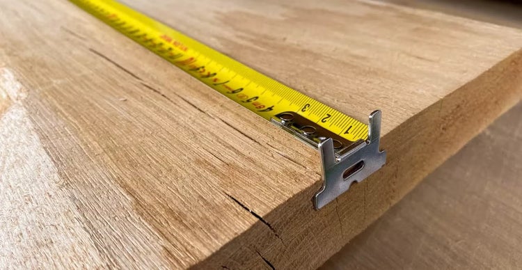 Ein Maßband liegt auf einem rohen Holzbrett aus Eiche um die Maße zu nehmen.