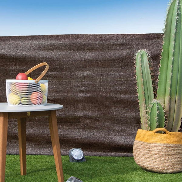 Brauner Sichtschutz aus Kunststoffgewebe auf einem sonnigen Balkon mit Kunstrasen, Holztisch, Obstkorb und einem großen Kaktus im Korbgeflecht.