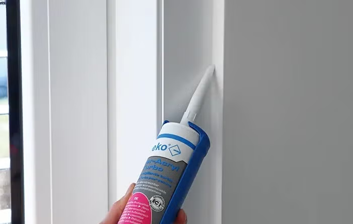 Eine Hand trägt mit einer Kartuschenpistole Eko Turbo Acryl Dichtstoff auf eine Fuge an einer Wand auf.