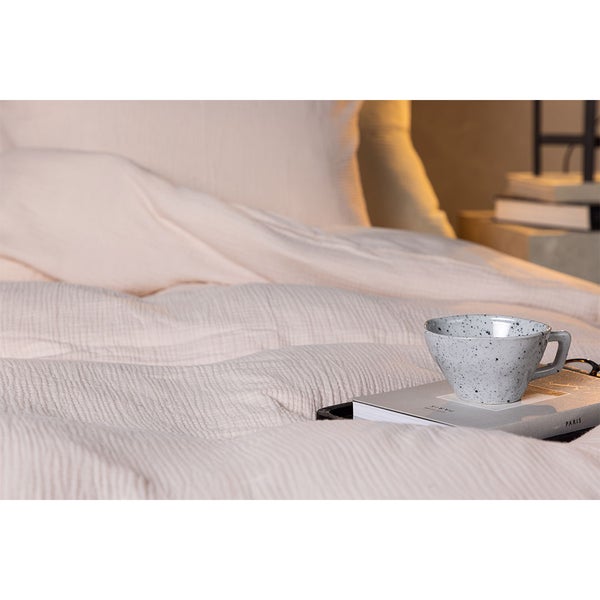 Nahaufnahme strukturierter Bettwäsche aus Musselin auf einem Bett mit einer Tasse auf einem Buch.