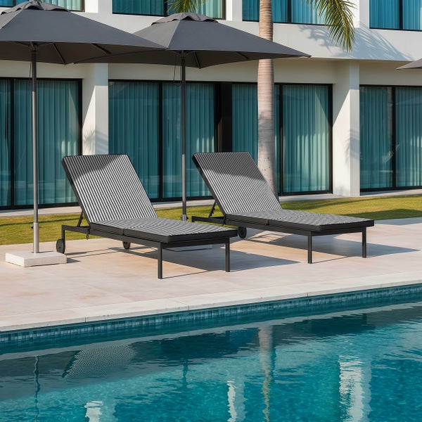 Zwei moderne Gartenliegen mit gestreiften Auflagen und zwei große Sonnenschirme am Rand eines Swimmingpools auf einer hellen Terrasse.