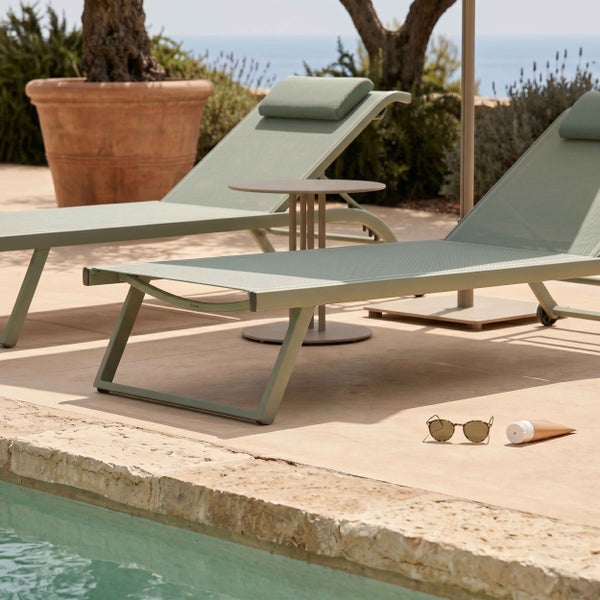 Helle Poolterrasse mit zwei modernen Gartenliegen aus Metall und Textilgewebe, einem runden Beistelltisch und einer Steinumrandung am Becken.