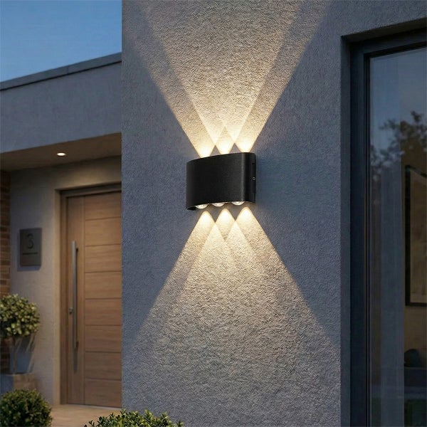 Moderne schwarze Außenwandleuchte an einer strukturierten Fassade mit Lichtstrahlen nach oben und unten in einem hellen Eingangsbereich.
