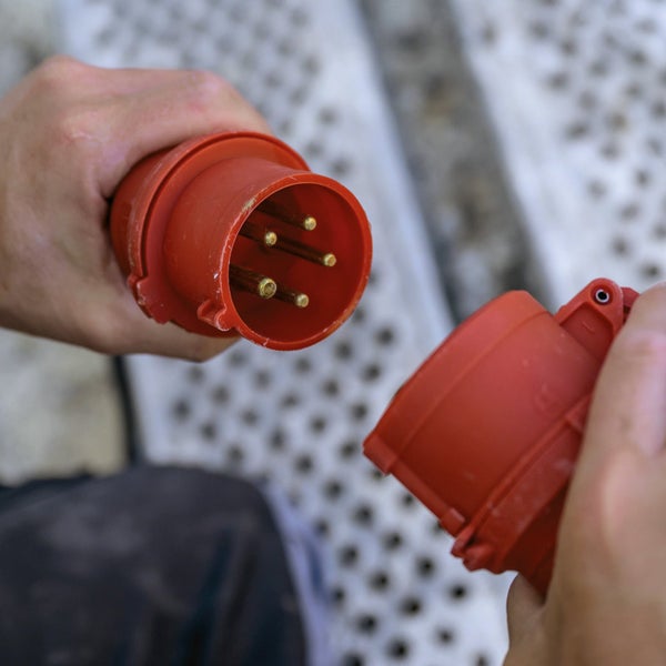 Eine Person hält einen roten Starkstromstecker und eine Kupplung in der Hand.