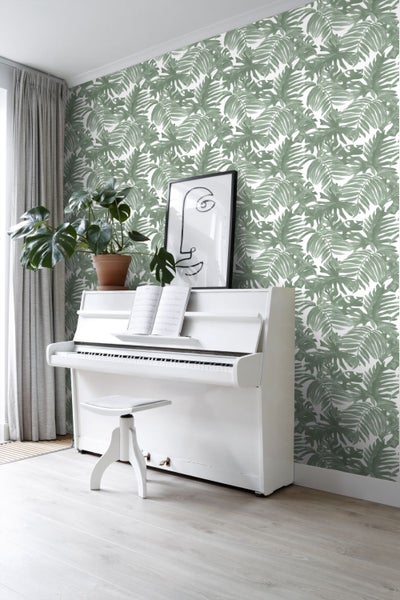 Heller Raum mit einem weißen Klavier, einem Hocker, Zimmerpflanzen und einer Wand mit Blattmuster-Tapete.