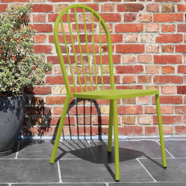 Moderner grüner Gartenstuhl aus Metall mit Sprossenlehne auf dunklen Terrassenplatten vor einer Ziegelwand neben einer Pflanze im Topf.