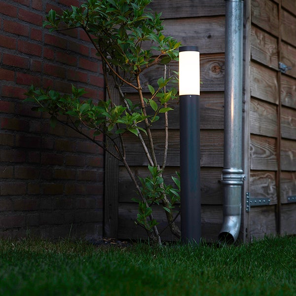 Eine modern beleuchtete LED-Wegeleuchte in einem Garten bei Nacht, platziert auf einer Rasenfläche vor einem Holzzaun und einem Busch.