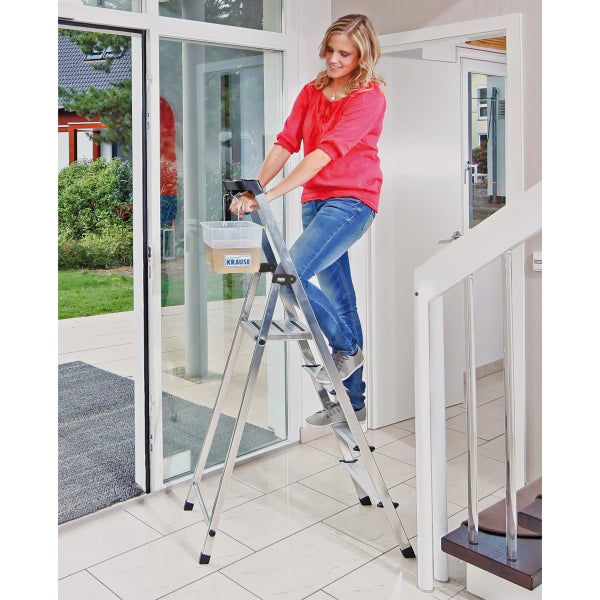 Frau auf einer Aluminium-Stufenleiter beim Fensterputzen im Haus.