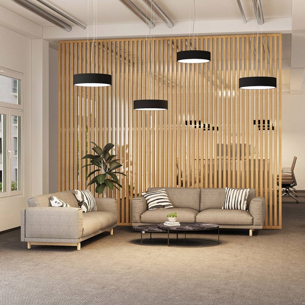Vier moderne schwarze Pendelleuchten über einem Sitzbereich mit grauen Sofas und einer Trennwand aus Holzlamellen in einem hellen Büro.