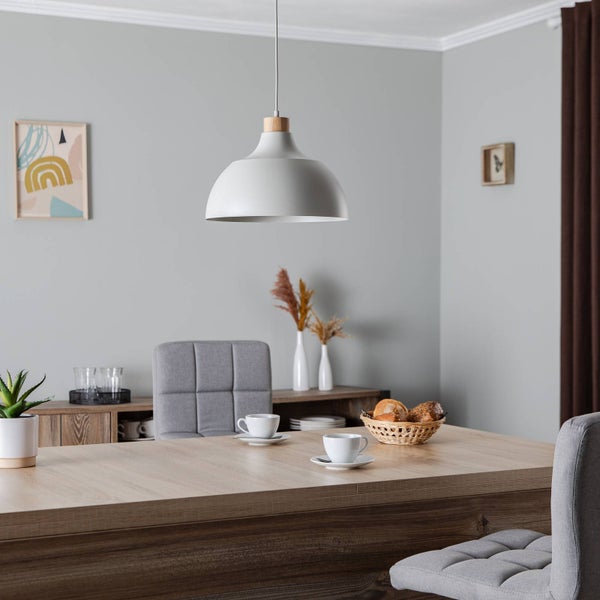 Moderne Pendelleuchte in Weiß mit Holzelement über einem Esstisch aus Holz mit grauen Stühlen in einem hellen, aufgeräumten Raum.