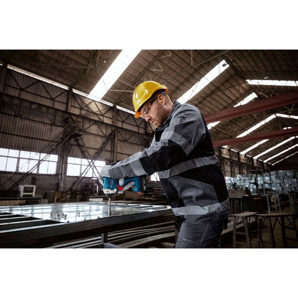 Ein Arbeiter mit Schutzhelm und Schutzbrille verwendet einen Akku-Schlagschrauber in einer Werkshalle.