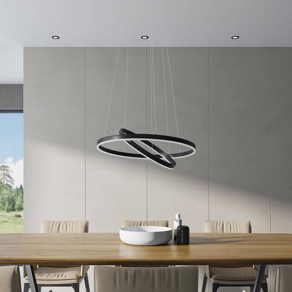 Modernes, helles Esszimmer mit einer schwarzen LED-Pendelleuchte aus zwei ineinandergreifenden Ringen über einem Holztisch mit beigen Stühlen.