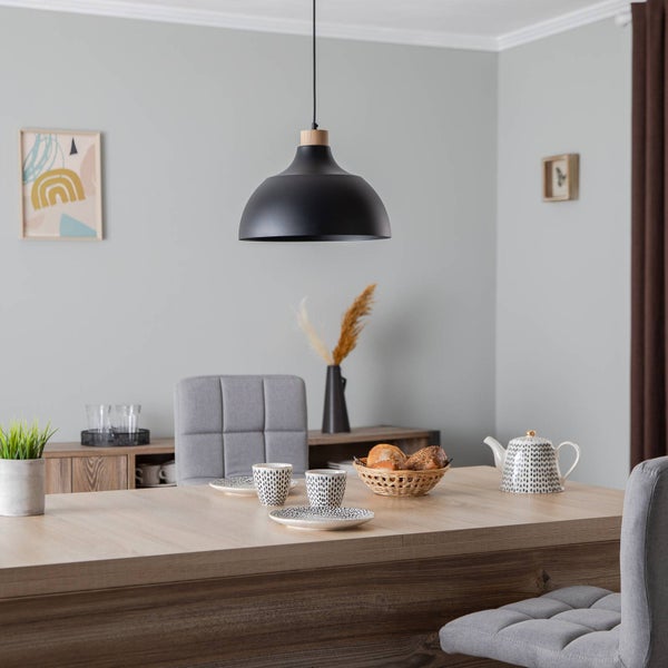 Schwarze Pendelleuchte aus Metall mit Holzdetail über einem Holzesstisch in einem hellen, modern eingerichteten Esszimmer mit grauen Stühlen.