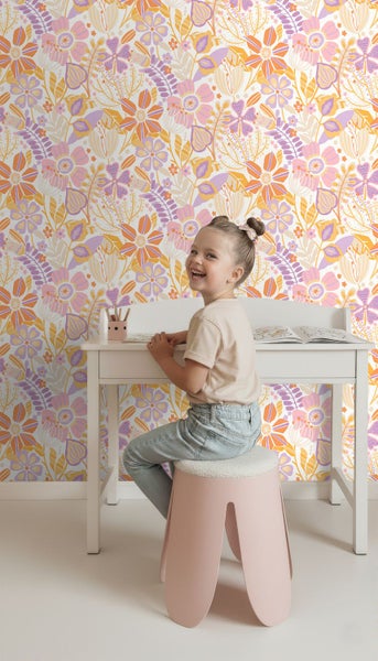 Kinderzimmer mit floraler Mustertapete in Rosa, Orange und Lila. Ein Kind sitzt an einem weißen Schreibtisch vor der gemusterten Wand.
