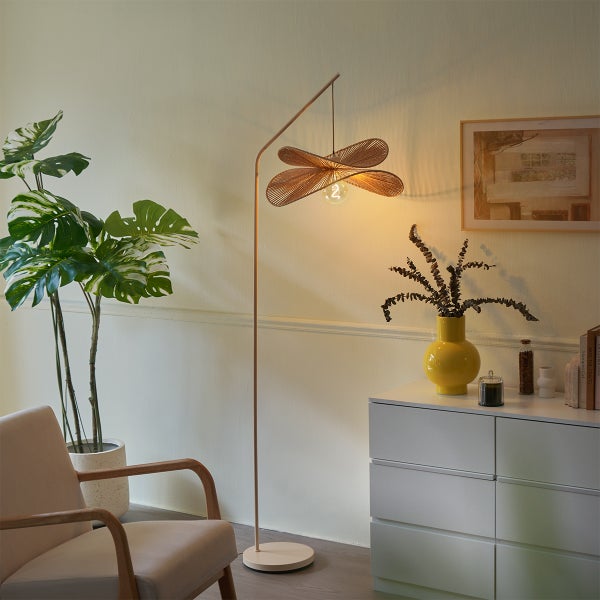 Moderne Bogenstehlampe mit geflochtenem Lampenschirm in einem Wohnraum mit Sessel, Pflanze und Kommode eingerichtet.