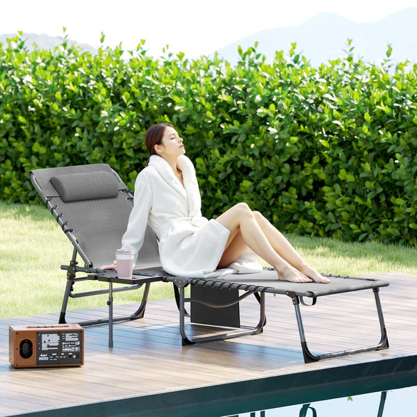Frau im Bademantel entspannt auf einer grauen Sonnenliege mit Kopfstütze und Ablagetisch auf einer Holzterrasse am Pool im Garten.