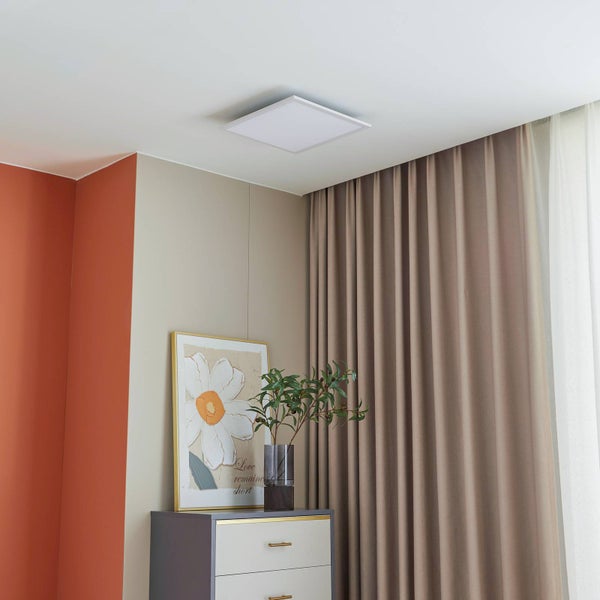 Quadratisches LED-Panel an der Decke in einem hellen, modern eingerichteten Raum mit beigen Vorhängen, Kommode und Wandbild.