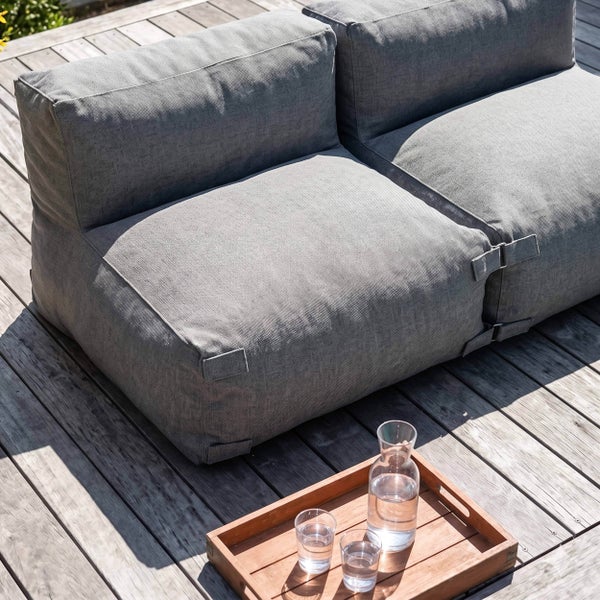 Graues modulares Lounge Sofa Element aus Stoff auf einer sonnigen Holzterrasse