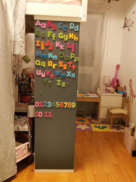 Graue Magnetwand im Kinderzimmer mit bunten Buchstaben und Zahlen an einem Hochbett montiert.