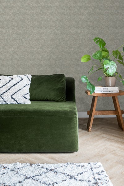 Einrichtungsansicht mit einem grünen Sofa, einem Holzhocker und einer Zimmerpflanze.