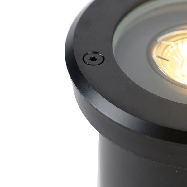 Nahaufnahme eines runden schwarzen Bodeneinbaustrahlers mit eingeschalteter Lichtquelle und einer Schraube am Gehäuserand.
