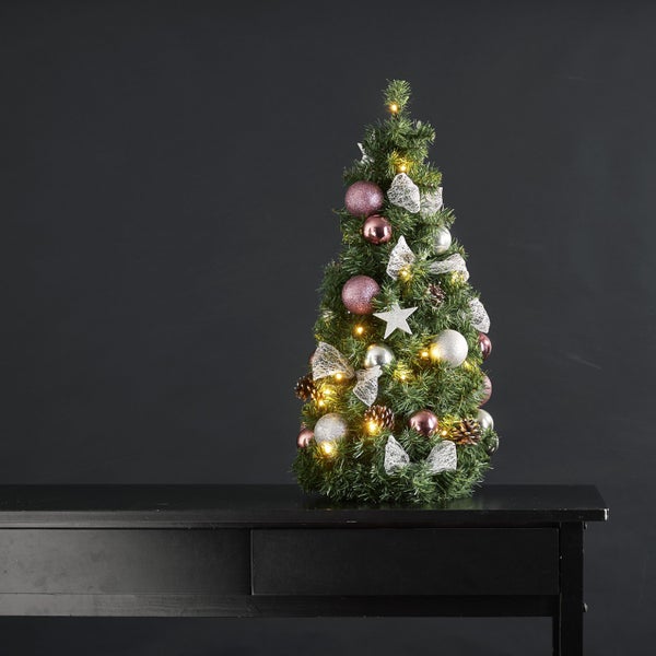 Dekorierter Weihnachtsbaum mit Kugeln, Schleifen, Tannenzapfen und Beleuchtung auf einem Tisch