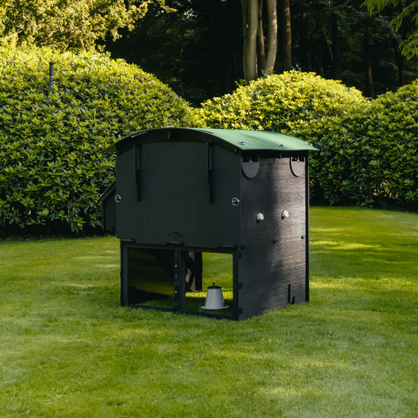 Moderner Hühnerstall aus recyceltem Kunststoff in Dunkelgrau mit grünem Dach, freistehend auf einer Rasenfläche im Garten.