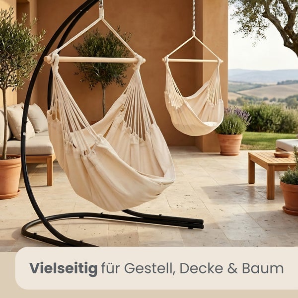 Hängesessel aus Stoff an einem Gestell und einer Deckenbefestigung auf einer hellen Terrasse mit Holzmöbeln und Pflanzen.