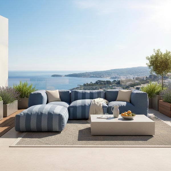 Moderne Terrasse mit einem blau gestreiften modularen Gartensofa, Hocker, hellem Couchtisch und Außenteppich mit Blick auf das Meer.