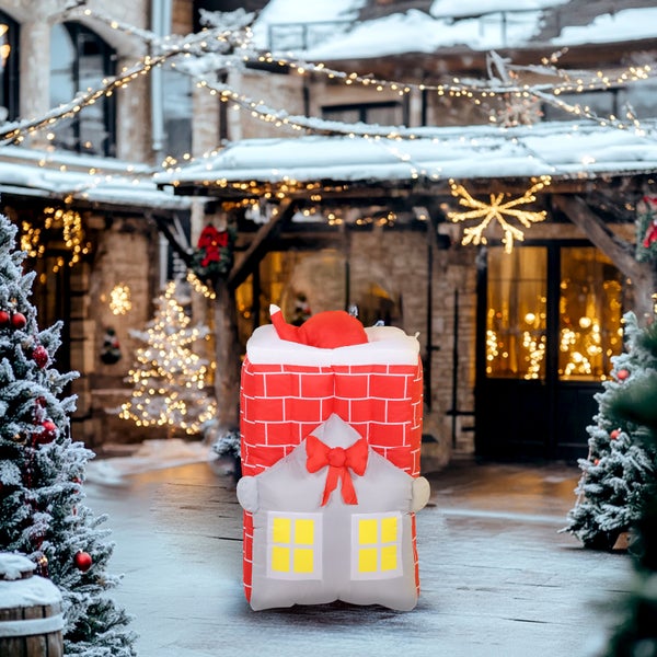 Aufblasbare Weihnachtsdekoration in Form eines Kamins mit Haus in einer verschneiten, festlich beleuchteten Außenanlage.