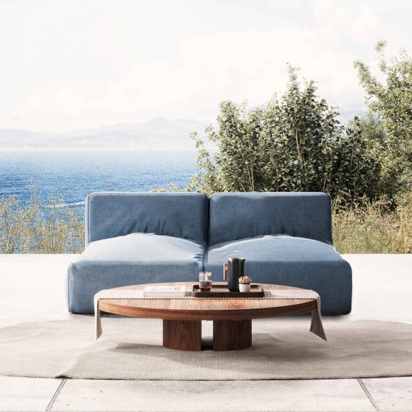 Blaue Outdoor-Lounge mit rundem Couchtisch aus Holz auf einer Terrasse mit Meerblick, helle und einladende Atmosphäre.