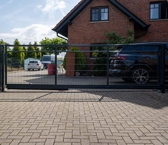 Schiebetor aus Metall vor einem Haus mit Fahrzeugen