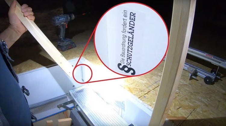 Hinweisaufkleber zur Bauordnung für ein Schutzgeländer an einer Bodentreppe während der Montage mit Holzleisten.