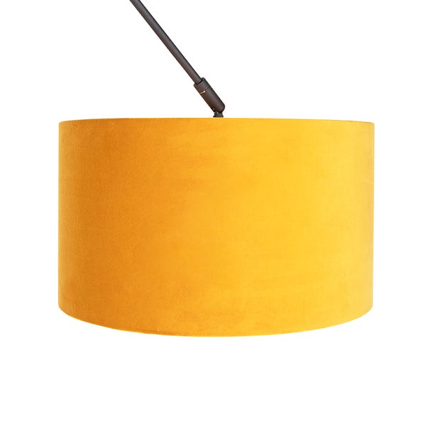 Zylindrischer Lampenschirm aus gelbem Samtstoff an einem dunklen Lampenarm.