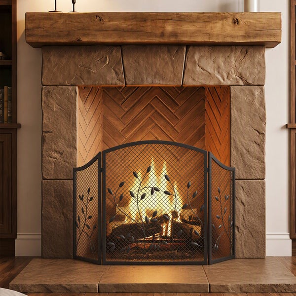 Rustikaler Steinkamin mit Holzbalkensims und dreiteiligem Funkenschutzgitter mit Blattverzierung vor brennendem Holzfeuer.