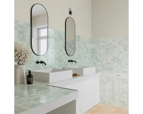 Modernes Badezimmer mit zwei weißen Aufsatzwaschbecken, ovalen schwarzen Spiegeln und hellen quadratischen Wandfliesen.