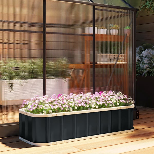 Schwarzes Hochbeet aus Metall mit rosa und weißen Blumen vor einem Gewächshaus auf einer Holzterrasse.