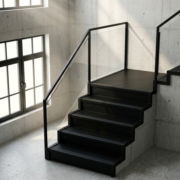 Moderne, schwarze Metalltreppe mit Glasgeländer in einem hellen Raum mit Sichtbetonwänden und großen Fenstern im Industriestil.