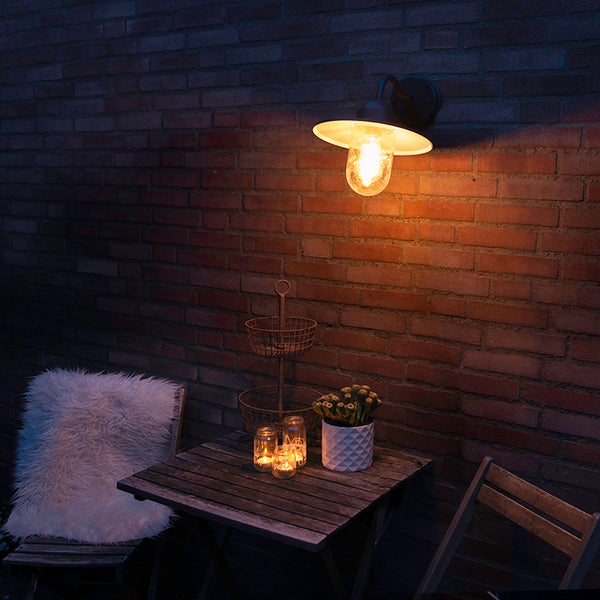 Außenbereich mit Wandleuchte, Tisch, Stühlen und Dekoration auf einer Terrasse bei Nacht