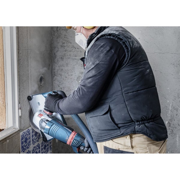 Eine Person benutzt eine Mauernutfräse mit Staubabsaugung zum Schneiden einer Wand.