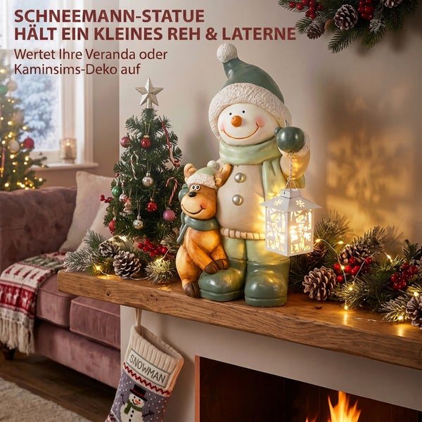 Schneemann Dekofigur mit Rentier und leuchtender Laterne als weihnachtliche Dekoration auf einem Kamin mit Tannenbaum und Weihnachtsstrumpf.