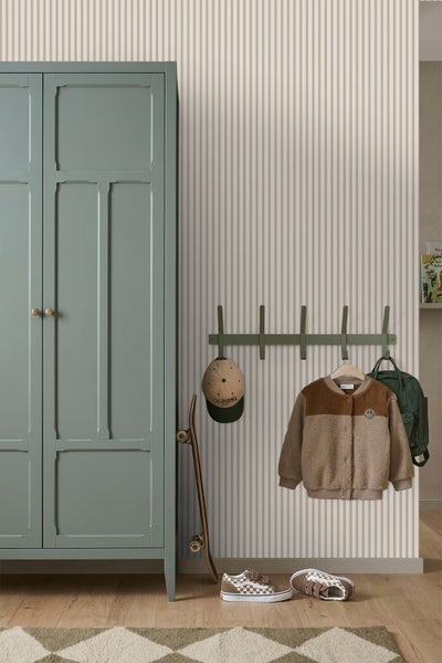Kinderzimmer mit grünem Kleiderschrank, gestreifter Tapete und einer Wandgarderobe mit Jacke, Mütze und Rucksack sowie einem Skateboard.