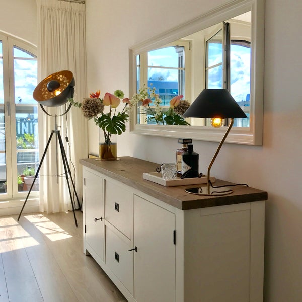 Wohnzimmer mit Sideboard, Tischleuchte, Stehlampe, Spiegel und Dekorationen.