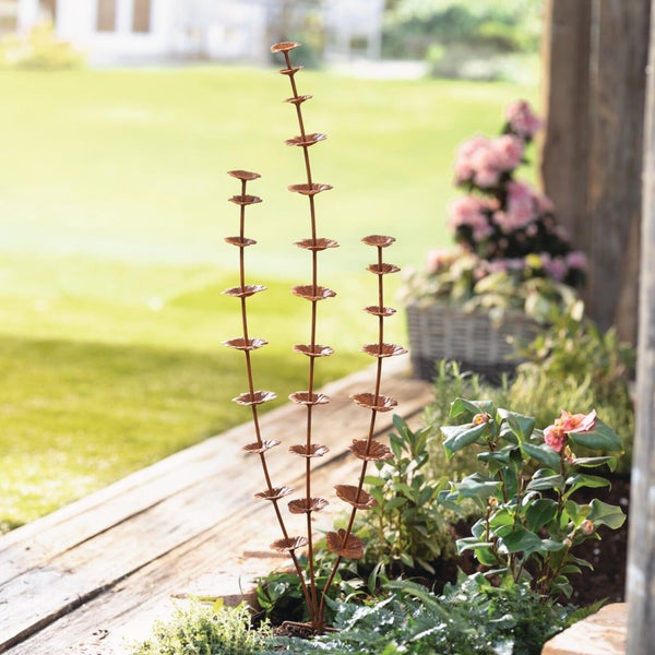 Dreiarmiger Gartenstecker aus Metall mit gestuften Schalen in einem bepflanzten Blumenbeet.