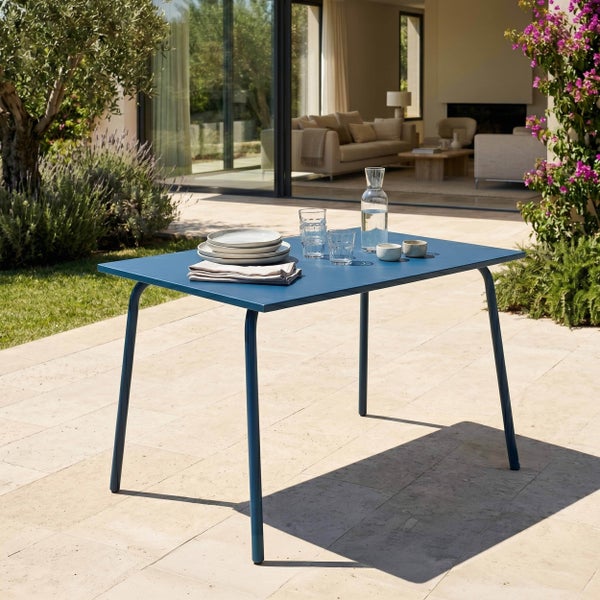 Moderner blauer Gartentisch aus Metall auf einer Terrasse, gedeckt mit Geschirr vor einer hellen Glasfront.