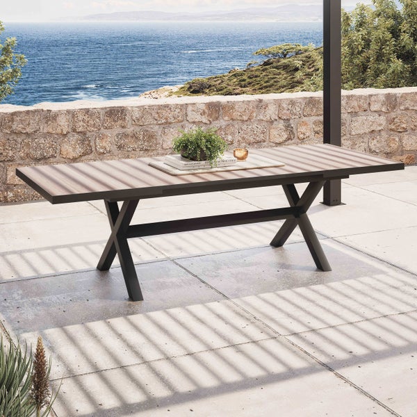 Moderner Gartentisch mit dunklem X-Gestell aus Metall und Tischplatte in Holzoptik auf einer Terrasse mit Meerblick.